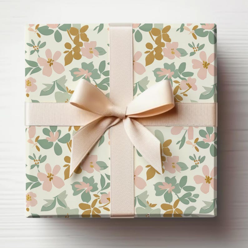 Op de afbeelding: Een cadeaudoos ingepakt in wit papier met een bloemenpatroon in roze, groene en gouden tinten. De doos is vastgebonden met een cr&egrave;mekleurig satijnen lint.