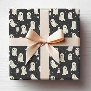 May include: A black gift box with a white ghost pattern and a beige ribbon bow. The box is wrapped in Halloween themed wrapping paper.