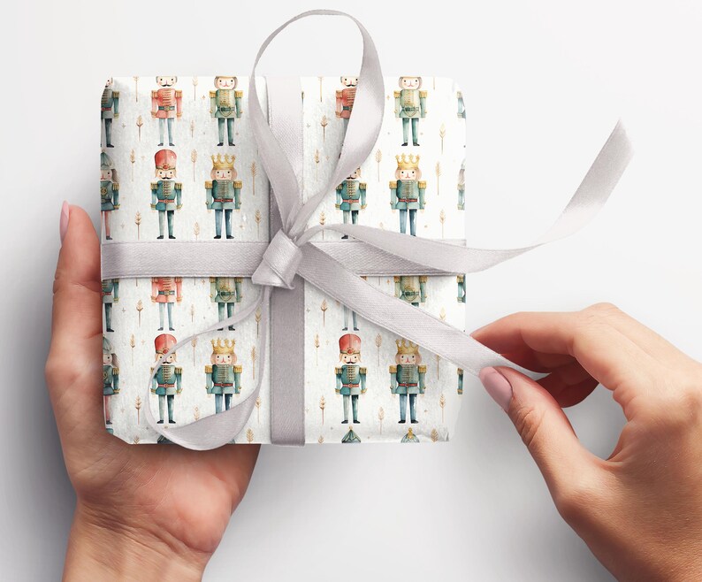 May include: A white gift box with a silver ribbon is wrapped in wrapping paper with a repeating pattern of watercolor nutcracker soldiers. The nutcracker soldiers are wearing blue and red uniforms with gold accents.