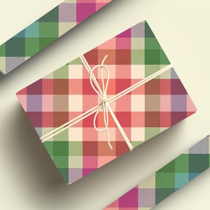 May include: A wrapped gift box with a colorful plaid pattern in shades of red, green, pink, and beige. The box is tied with white twine. Two additional pieces of the plaid paper are also visible.