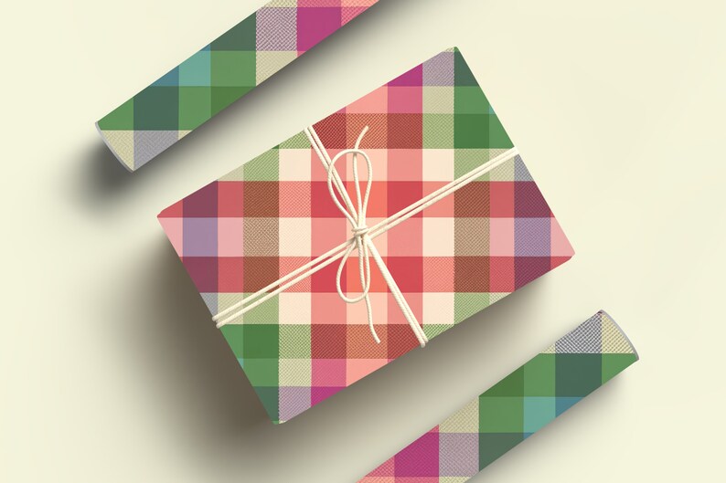 May include: A wrapped gift box with a colorful plaid pattern in shades of red, green, pink, and beige. The box is tied with white twine. Two additional pieces of the plaid paper are also visible.