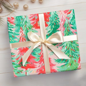 May include: A pink gift box with a white ribbon and bow. The box is wrapped in paper with a pattern of green and red Christmas trees.
