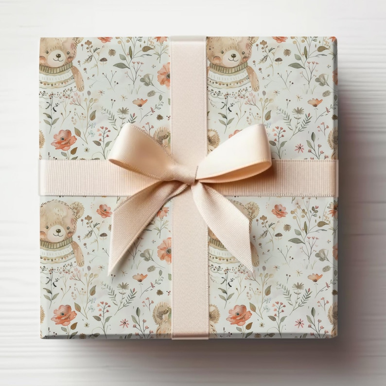 May include: A gift box wrapped in white paper with a brown bear and floral pattern. The box is tied with a light pink ribbon.