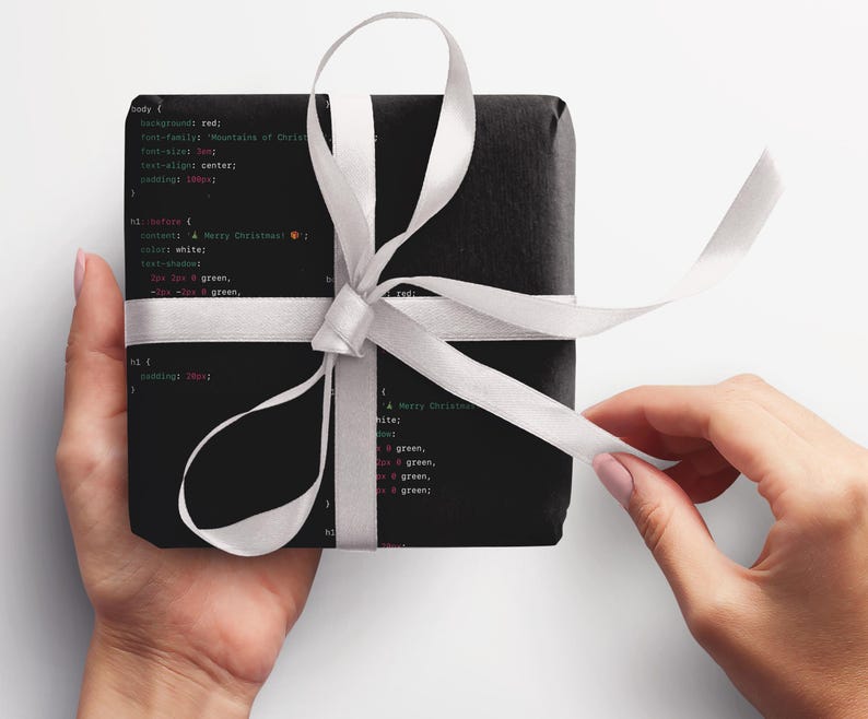 May include: A black gift box wrapped with a white ribbon and tied in a bow. The box is covered in code with the text "Merry Christmas!" in green and red.