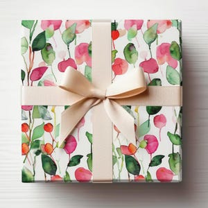 May include: A gift box wrapped in white paper with a pink and green watercolor floral pattern. The box is tied with a cream-colored satin ribbon.