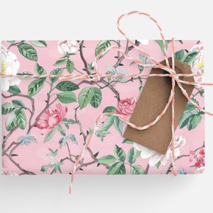 May include: A wrapped gift with a floral pattern featuring pink roses, white flowers, and green leaves on a pink background. The gift is tied with a white and peach twine and a brown tag.