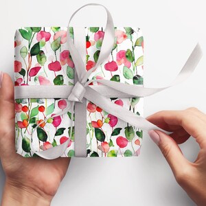 May include: A white gift box wrapped in floral patterned paper with pink, red, and green watercolor flowers. A silver ribbon is tied around the box.