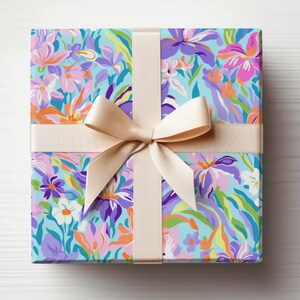 May include: A gift box wrapped in floral patterned paper with a light blue background. The paper features a variety of colorful flowers, including pink, purple, orange, and yellow. The box is tied with a cream-colored ribbon.