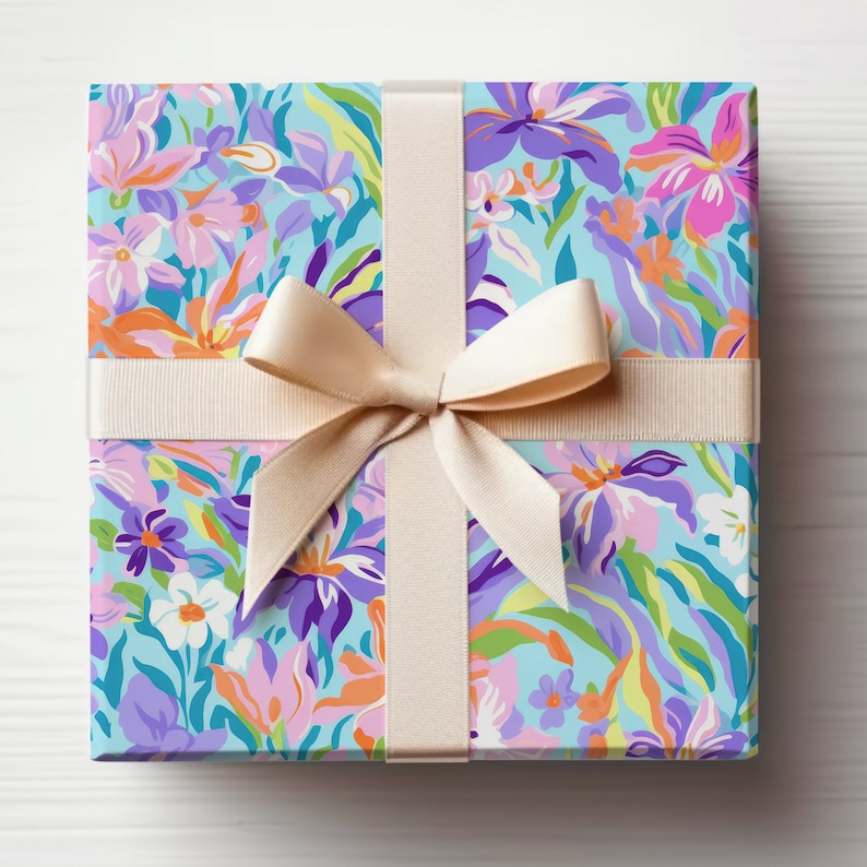 May include: A gift box wrapped in floral patterned paper with a light blue background. The paper features a variety of colorful flowers, including pink, purple, orange, and yellow. The box is tied with a cream-colored ribbon.