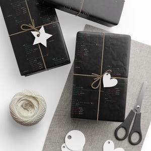 May include: Three black gift boxes wrapped in paper with code printed on it. The boxes are tied with twine and decorated with white paper stars and hearts.