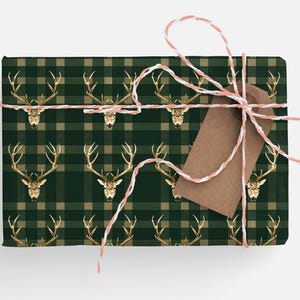 May include: A green and tan plaid gift wrap with a gold stag head pattern. The gift is tied with a white and pink twine and a brown gift tag.