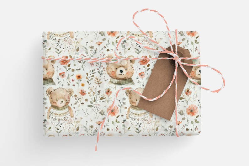 May include: A white gift wrap with a repeating pattern of brown bears wearing sweaters and pink flowers. The gift is tied with a white and pink twine and a brown tag.