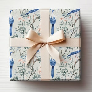 May include: A gift box wrapped in white paper with a blue and white bird pattern. The box is tied with a beige ribbon.