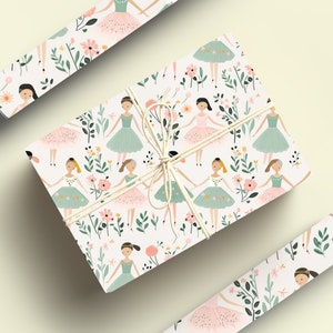 May include: White gift wrap with a repeating pattern of ballerinas wearing pink and green tutus with floral accents. The gift wrap is rolled up and tied with twine.