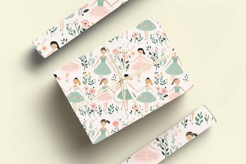 May include: White gift wrap with a repeating pattern of ballerinas wearing pink and green tutus with floral accents. The gift wrap is rolled up and tied with twine.