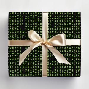 Peut inclure: Un coffret cadeau carr&eacute; envelopp&eacute; dans du papier noir avec un motif de code binaire vert. Un ruban et un n&oelig;ud en satin dor&eacute; sont attach&eacute;s autour de la bo&icirc;te, cr&eacute;ant une pr&eacute;sentation festive.
