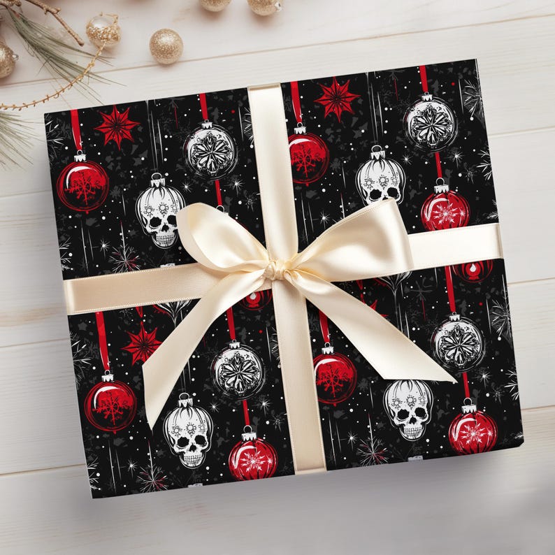 May include: Black and white skull Christmas baubles with red and white snowflake accents on a black background. The gift is wrapped with a cream-coloured ribbon.