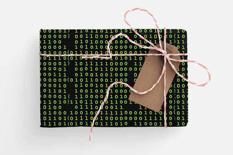 Peut inclure: Un cadeau emball&eacute; avec du papier cadeau noir &agrave; code binaire et une &eacute;tiquette marron. Le cadeau est nou&eacute; avec de la ficelle rose et blanche. Le code binaire est en vert.