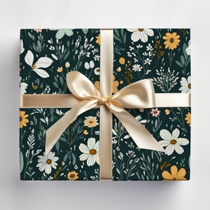 May include: A gift box wrapped in dark green wrapping paper with a floral pattern. The paper features white, yellow, and pink flowers with green leaves. A gold ribbon is tied around the box.