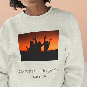 May include: A light gray sweatshirt with a graphic of three people silhouetted against an orange sunset. The text "Go where the people dance..." is printed below the graphic.