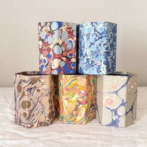 May include: Five hexagonal containers featuring distinct marbled paper patterns. The top row includes a red, blue, and grey design alongside a blue and white pattern. The bottom row features a brown, yellow, and pink, and a grey and blue design.