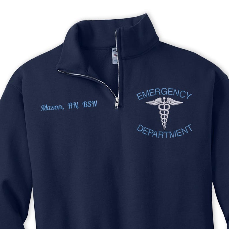 Pu&ograve; includere: Una felpa blu navy con zip a un quarto con il testo "EMERGENCY DEPARTMENT" e un simbolo di caduceo ricamato sul petto destro. Il testo "Mason, RN, BSN" &egrave; ricamato sul petto sinistro.