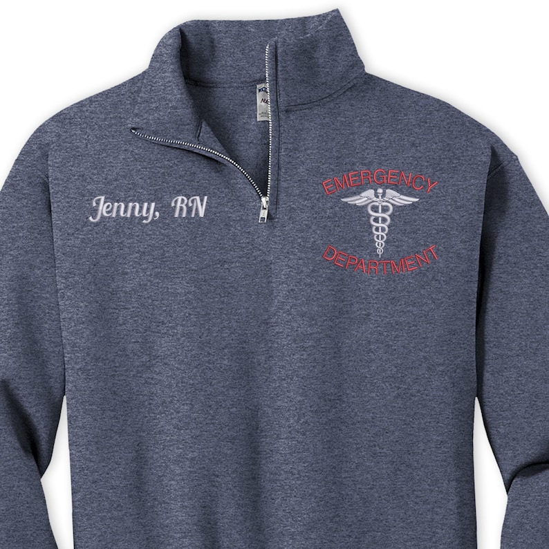 Pu&ograve; includere: Una felpa blu scuro con zip 1/4 con il testo "Jenny, RN" ricamato sul petto sinistro e "Emergency Department" con un simbolo di caduceo ricamato sul petto destro.