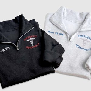 Pu&ograve; includere: Due felpe grigie e nere con zip a un quarto di giro con il testo "Emergency Department" e un simbolo medico ricamato sul davanti. Una felpa ha il testo "Jenny, RN" e l'altra ha il testo "Mason, RN, BSN".