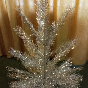 Può includere: Un albero di Natale in tinsel argentato con un tronco centrale e rami radianti. L'albero ha una forma conica ed è decorato con tinsel scintillante, creando un aspetto festoso e luccicante. L'albero è alto circa 91 cm.