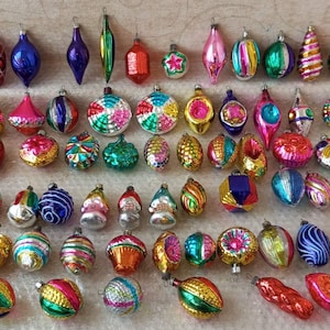 Può includere: Una vasta collezione di decorazioni natalizie in vetro vintage di varie forme, tra cui sfere, gocce e puntali. Gli ornamenti presentano un'ampia gamma di finiture metalliche, lucide e glitterate nei colori rosso, blu, verde, oro e rosa.