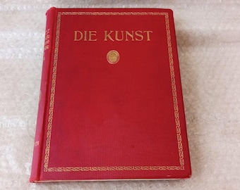 Puede incluir: Un libro rojo titulado "DIE KUNST" en letras doradas. El libro tiene un borde decorativo dorado y un pequeño emblema en el centro. El libro está cerrado y parece estar en buen estado.