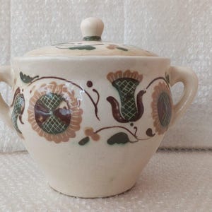 Può includere: Una zuccheriera in ceramica bianca con coperchio, con un motivo floreale in tonalità di marrone, verde e bianco.