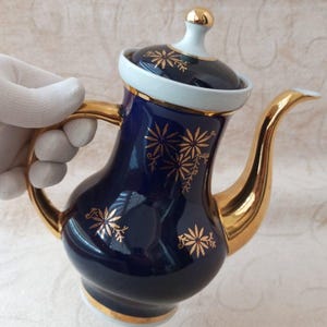 Könnte beinhalten: Eine kobaltblaue Porzellan-Teekanne mit goldenen Verzierungen und floralen Mustern. Die Teekanne hat einen Deckel mit einem goldenen Knopf und einem goldenen Ausguss.
