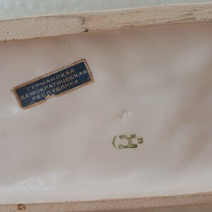 May include: A white ceramic figurine with a blue label that reads "German Democratic Republic". The figurine has a green mark that reads "(36".