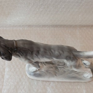 May include: A porcelain figurine of a greyhound dog running, with a white tail and base. The dog is in a hunting pose, with its head turned to the side.