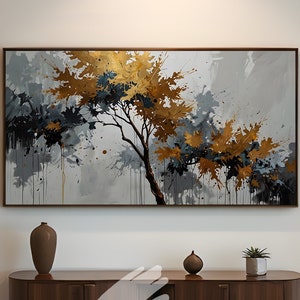Puede incluir: Impresión artística abstracta de un árbol con hojas doradas y azul marino sobre un fondo gris y blanco. La obra de arte está enmarcada y cuelga sobre una consola de madera de estilo moderno de mediados de siglo. La mesa tiene un jarrón marrón, una pequeña esfera decorativa y una planta en maceta.