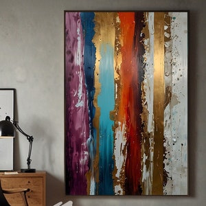 Op de afbeelding: Abstract schilderij met verticale strepen in tinten van paars, blauw, turquoise, oranje, rood, goud en wit. Het schilderij is ingelijst en hangt aan een muur in een kamer met een houten vloer en een zwarte leren fauteuil.