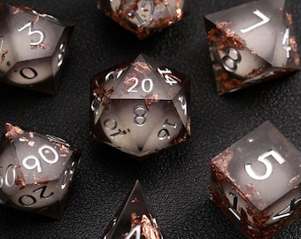 May include: Set of seven polyhedral dice for tabletop games. The dice are a translucent gray with copper-colored inclusions and white numbering. The dice include a D4, D6, D8, D10, D12, D20, and a percentile die.