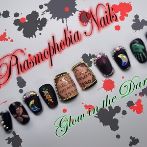 May include: Black and white glow-in-the-dark nail art with a Ouija board design. The nails are decorated with rhinestones and a crescent moon design. The text on the nails reads "YOU, ABC, DEF, NO, PQR, 123, 456, 7890".