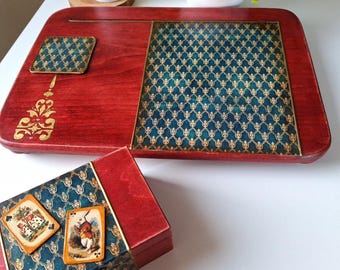 Puede incluir: Un escritorio portátil de madera roja con una inserción estampada en verde azulado y dorado y un posavasos a juego. Un diseño dorado decorativo está en el escritorio. También se muestra una caja de madera roja con una parte superior estampada en verde azulado y dorado y dos naipes.