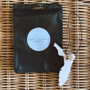 May include: A white wooden Florida state-shaped ornament with a small white bead and black string. The ornament is next to a black package with a white circle and the text "THREE ROOKER collections."
