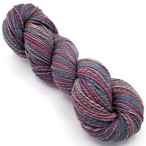 May include: A skein of yarn in shades of purple, teal, and beige. The yarn is tightly twisted, showing a blend of colors throughout. The yarn appears soft and suitable for knitting or crocheting projects.