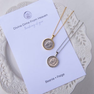 May include: Two silver necklaces with a dime pendant. The dimes are encased in a silver frame. The necklaces are on a white card with the text "Divine Dime From Heaven...thinking of you" and "Beanie + Paige".