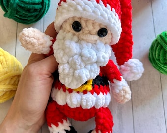 May include: A crocheted Santa Claus toy with a red hat, white beard, and black boots. The toy is made with soft, plush yarn and has a friendly expression.