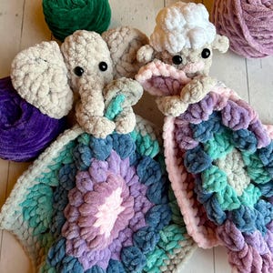 May include: A crocheted elephant and lamb security blanket with a multi-coloured, textured design. The blanket is made with soft, chunky yarn in shades of pink, purple, blue, and green.