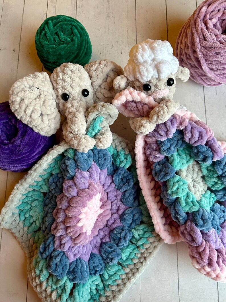 May include: A crocheted elephant and lamb security blanket with a multi-coloured, textured design. The blanket is made with soft, chunky yarn in shades of pink, purple, blue, and green.