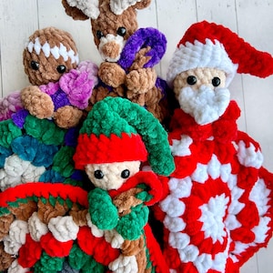May include: Five crocheted Christmas ornaments, including a gingerbread person, a reindeer, Santa Claus, and an elf, are arranged on a white crocheted blanket. The blanket is made with a variety of colors, including red, green, white, and brown.