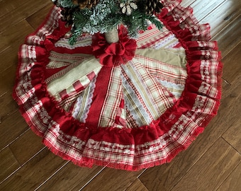 May include: A red and white plaid Christmas tree skirt with a burlap bow and lace trim. The skirt is made of fabric scraps and has a rustic, farmhouse style.