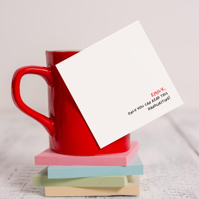 Op de afbeelding: Een rode mok met een witte kaart erop. Op de kaart staat in rood en zwart "Emily, only you can read this handwriting!" geschreven.