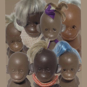 Puede incluir: Una colección de muñecos de mono vintage con piel marrón y varios peinados, incluyendo gris, rubio y azul. Algunos muñecos tienen pequeños lazos o collares decorativos. Los muñecos están dispuestos muy juntos.